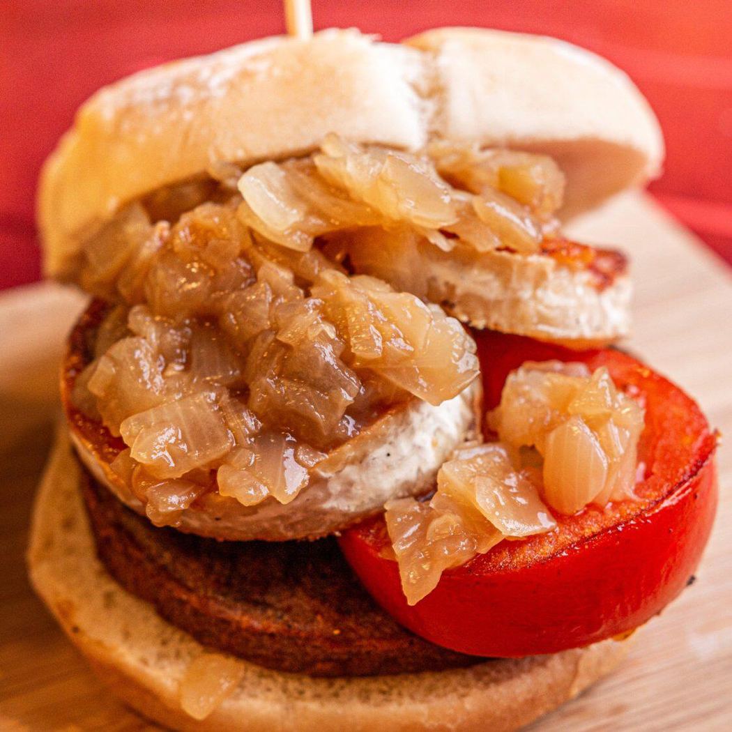 Hamburguesa jugosa con cebolla caramelizada y tomate asado, servida con patatas.