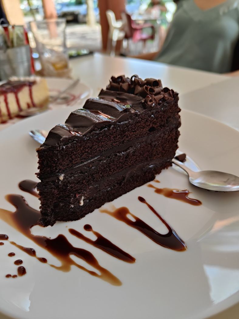 Porción de tarta de chocolate intensa con ganache y virutas de chocolate negro.